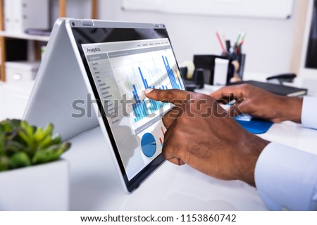 Businessman's Hand Pointing On Laptop Screen Showing Graph Over The Desk Royalty-Free Stock Photo #1153860742