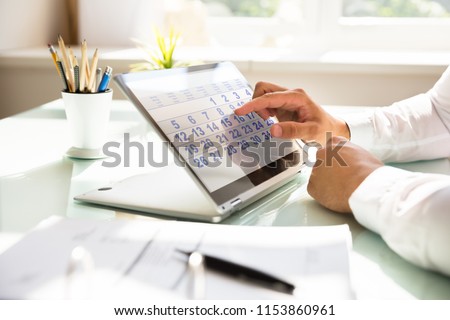 Close-up of a businessman's hand using calendar on laptop over desk