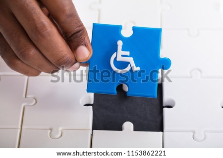 A Person's Hand Holding A Piece Of Blue Jigsaw Puzzle With Disabled Wheelchair Icon