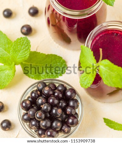 Currant smoothie decorated with fresh green mint leaves and raw ripe berries on yellow pastel background - transparent jars of summer blended vitamin cocktail for healthy food concept.