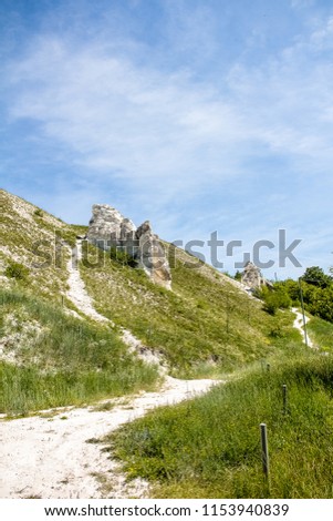 Beautiful scenery, chalk mountains stick out of the earth against the background of blue sky and green grass.