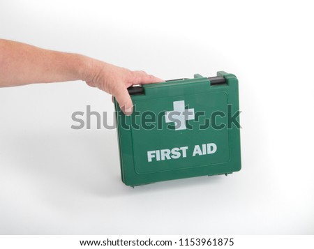 Male hand holding a green first aid box. UK. Green with white cross an text.