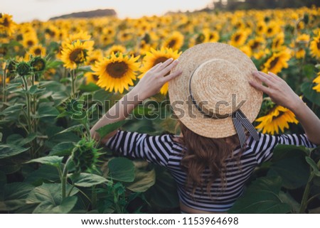 woman in black and white stripes t-shirt. straw hat on girl. field with blooming sunflower. young  girl in field with yellow sunflowers. lifestyle , ideal for advertising and photo sun shines bright 