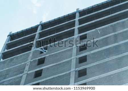 Multi-storey under construction building and construction crane on the background of clear sky.