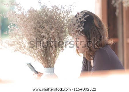 side view of Asian woman, who holding a smart phone in her hand. a photo take through a mirror, blur background.  concept for freelance, independent entrepreneur.