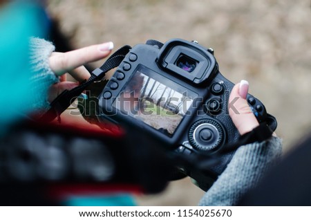 girl is looking at the frame on the camera screen. A girl photographer with a French manicure in a park in the fall.