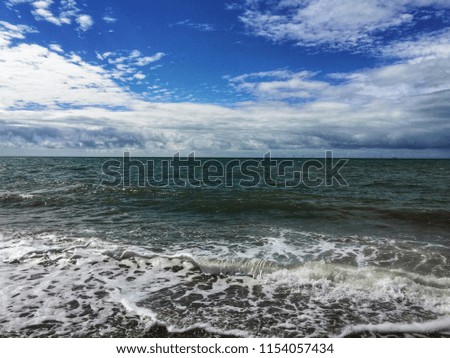 Pebble beach with green waves and foam under a cloudy sky blue sky