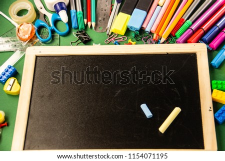 Felt pens, pencils, paperclips, crayons, rulers, glue, corrector marker and drawing board on a green background