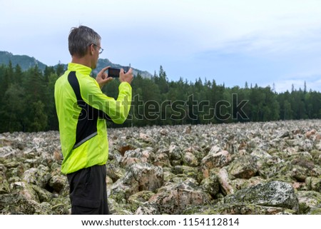 Man hiker on the stone river is taking a pictures, very beautiful and picturesque mountain landscape in the national park of nature Taganay, Russia, the Ural Mountains. View from the mountain