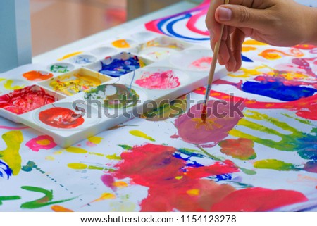 Closeup of kid's hand paints a picture of paint brush in hand with color palette.
Children's creativity.
