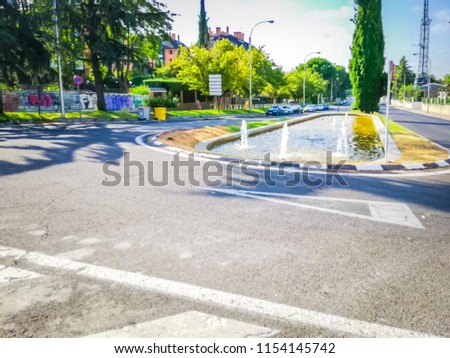 A small water fountain located in the middle of the well known Arturo Soria street next to the traffic circle intersecting with San Luis street in Summer in the north of Madrid, Spain, Europe