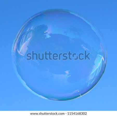 A close-up photograph of a floating soap bubble in motion in front of a clear blue sky.