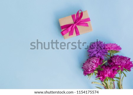 Bouquet with pink flowers with gift box on blue background empty space for your text, top view
