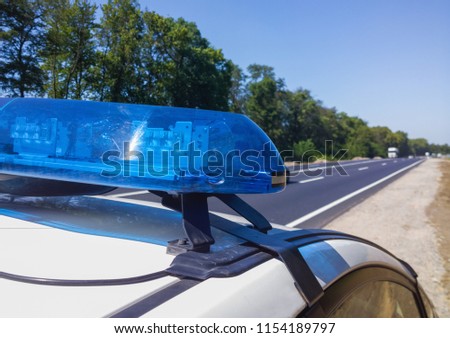 Blue flashing lights on the roof of a police car on the background of a high-speed road. Selective focus, close-up.