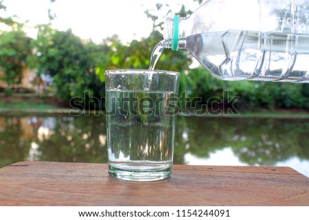 Close up pouring purified fresh drink water from the bottle on wooden table with nature background