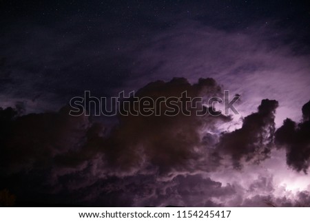 A lightning storm ignites clouds while stars can be seen