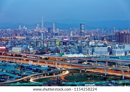 A panorama of Taipei City at dusk, the vibrant capital of Taiwan, with the landmark 101 Tower standing among skyscrapers in downtown & busy car trails on Xizhi-Wugu Elevated Highway under twilight sky