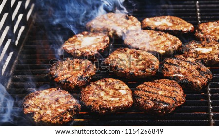 Preparing delicious hamburgers on the outdoor grill for family lunch. Conceptual picture of grilled burgers at fire flame. Hamburger patties turn over on the grill.