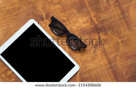 White tablet with black blank screen and glasses on wooden background. Flat lay. Copyspace concept