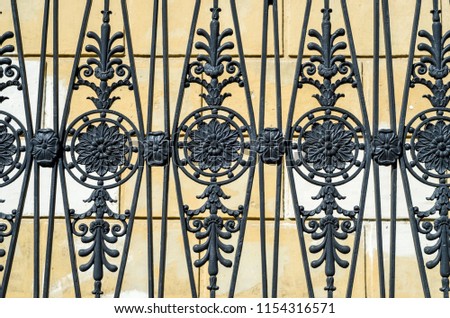 Black wrought iron grill on a yellow background. Historical grid with vegetative ornament.