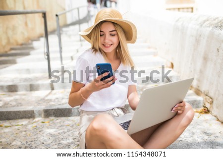 Pretty girl working with laptop sitting on stairs of city street.