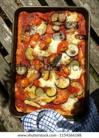 Close up  from above on italian  freshly home made organic vegetarian pizza courgette onion capers tomato pepper and other vegetables mozzarella on vintage wood table background outdoors tea towel