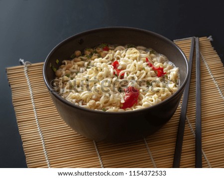 Instant noodles with red pepper in a ceramic bowl and black chopsticks on a bamboo mat