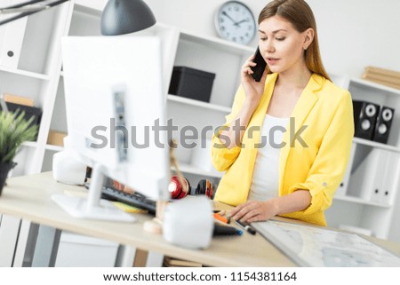 A young girl is standing near a table, talking on the phone and working with a computer. Before the girl on the table is a magnetic board
