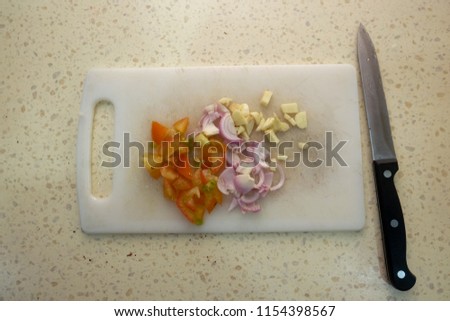 A flatlay picture of onion, garlic and tomato been cut for cooking.