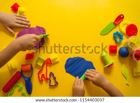 The child molds from colored plasticine. Yellow background. Materials and tools for modeling. Children's hands.