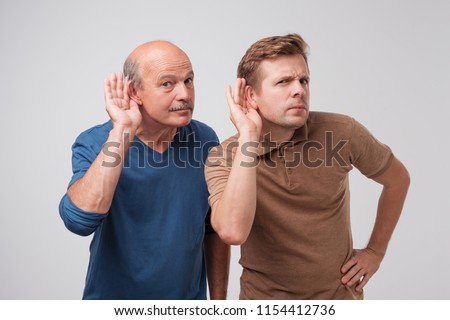 Two caucasian men hearing with hand on ear isolated on a white background. Please speak loudly. Having problem with hearing Royalty-Free Stock Photo #1154412736