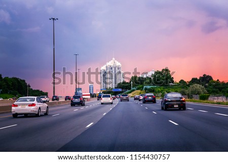 Night traffic. Cars on highway road at sunset evening in typical busy american city. Beautiful amazing night urban view with red, yellow and blue sky clouds. Sundown in downtown.