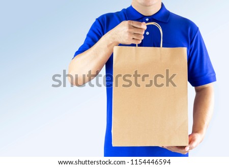 Delivery man in blue uniform and holding paper bag with delivering package on gray background. Concept fast food delivery service or order online shopping and express delivery.