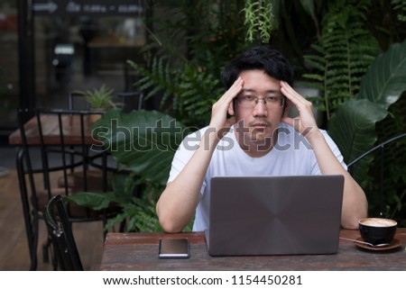 Asian businessman or student in casual white shirt expressing stress and trouble by facepalm and crazy face and hands while working in green garden coffee shop. Nature, cafe and business concept.