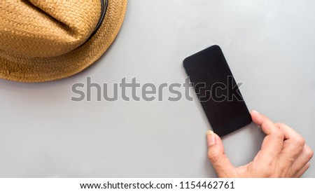 Hat wicker and smartphone with hand on gray background business concept