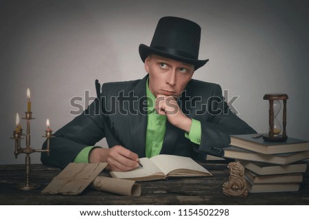 Pensive man in bowler hat and suit is sitting by table and holding a feather in pen in his hand. Writer, author, detective or spy agent concept.