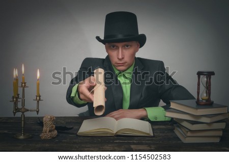 Man in bowler hat and suit is sitting by table and showing in hands a document scroll. Writer, author, detective or spy agent concept.