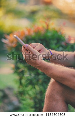 Modern man sitting in the tropical garden and using cellphone.