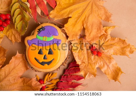 Halloween holiday - traditional sweets. Gingerbread pumpkin with a smile on the background of autumn leaves and kraft paper. Background image for inserting text.
