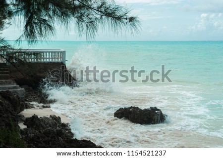 Blue waves break on the coastal rocks. Salt water spray in the light of the sun. Beach on Zanzibar island, Tanzania.