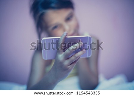 Little girl lying on bed and using smart phone late at night. Copy space. Close up. Focus is on hands.