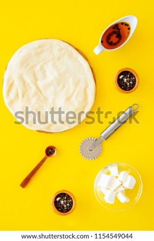 Raw rolled out pizza dough near cheese mozzarella, olive oil, spices, knife for pizza on yellow background top view mockup