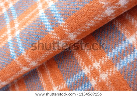 woolen fabric in a cage close-up gray orange stripes squares drape nap vintage coat plaid background for decor rolls cloth folds on fabric natural material