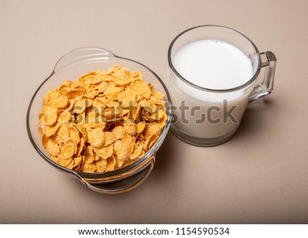 cornflakes in a glass plate a cup of milk on a gray background.