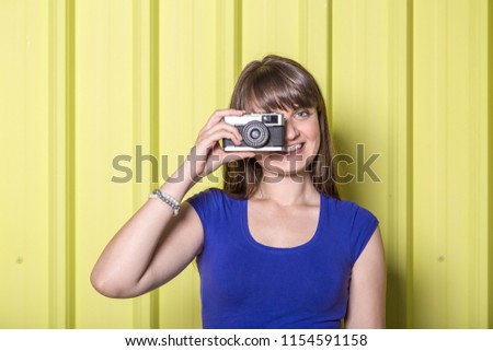 Beautiful woman holding vintage camera against yellow wall.