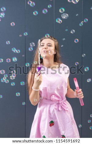Beautiful young girl blowing soap bubbles against gray background.