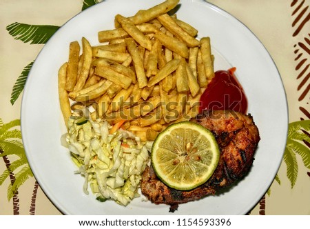 French fries, grilled fish, cabbage salad, ketchup, lime on a white plate. African style. Top view. Close up. Beautiful image. Food Photography.
