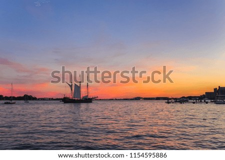 Lake Ontario with silhouettes of boats , ships, and Toronto West in the background at sunset.