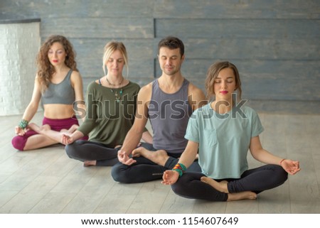 Group of young sporty people practicing yoga lesson, sitting in Sukhasana pose with closed eyes, working out, man and women training in sport club after work, close up,