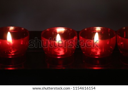 View of a red candles row in a church. Black dark background. Abstract picture with circular shapes and several flames. Colorful candlelight image. Contrasted colors.